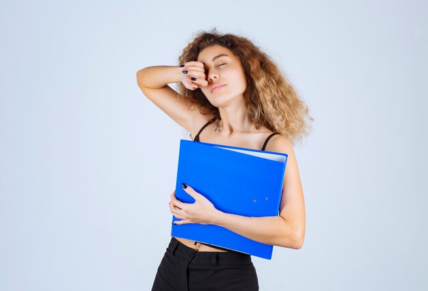 La fille blonde avec un dossier bleu a l'air endormie et fatiguée.