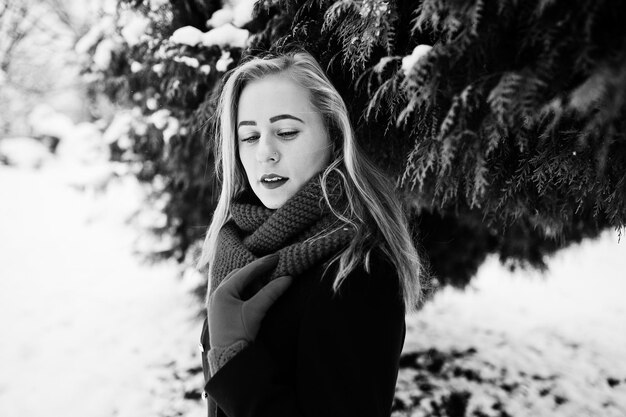 Fille blonde en écharpe rouge et manteau marchant au parc le jour de l'hiver