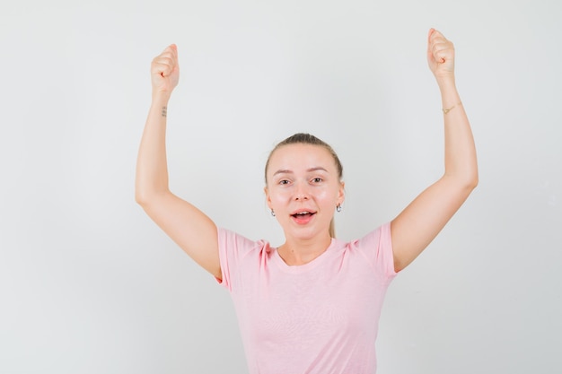 Fille blonde faisant semblant de tenir ou de montrer quelque chose en t-shirt, pantalon et à la joyeuse vue de face.