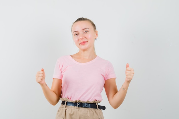 Fille blonde faisant semblant de tenir quelque chose en t-shirt, pantalon et regardant jolly, vue de face.