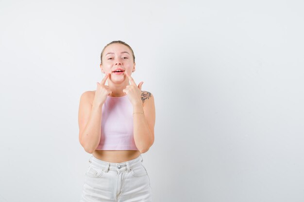 La fille blonde fait le sourire avec ses doigts sur le fond blanc