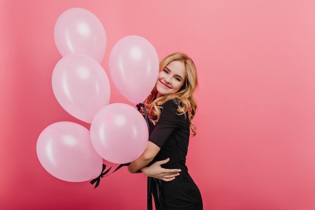 Fille blonde heureuse avec un sourire heureux debout avec un gros bouquet de ballons. Heureuse dame caucasienne bouclée en attente de fête d'anniversaire.