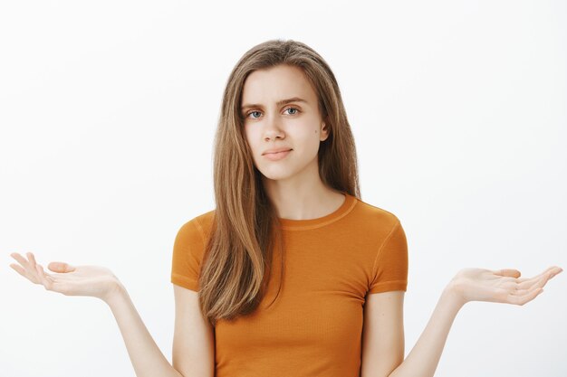 Fille blonde insouciante et confuse à la non amusée et haussant les épaules, alors quel geste