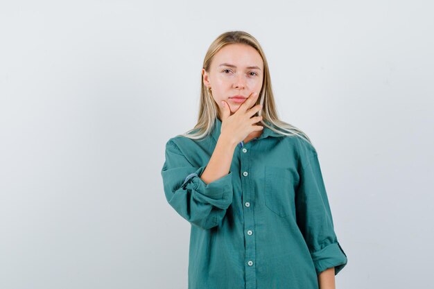 Fille blonde mettant la main sur le menton en chemisier vert et l'air sérieux.