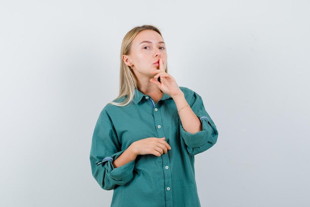 Photo gratuite fille blonde montrant un geste de silence en blouse verte et à la radieuse