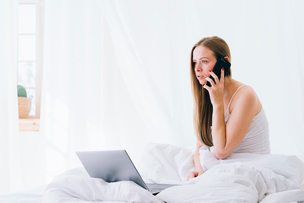 Fille blonde avec un ordinateur portable sur le lit