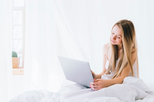 Fille blonde avec un ordinateur portable sur le lit