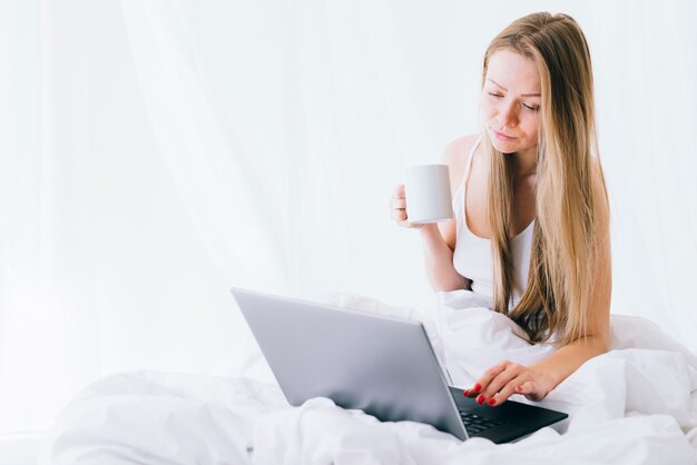 Fille blonde avec un ordinateur portable sur le lit