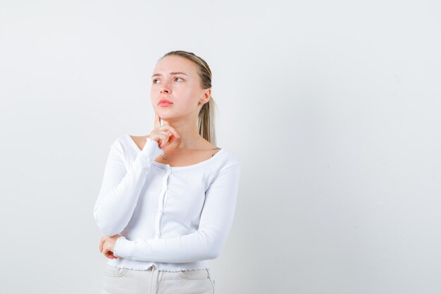 La fille blonde pense à n'importe quoi sur le fond blanc