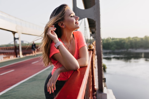 Fille blonde positive écoute de la musique après la formation. Superbe femme caucasienne relaxante en bon matin d'été.