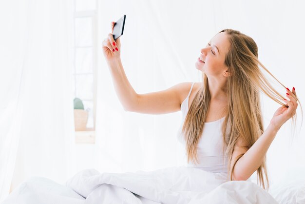 Fille blonde prenant selfie sur le lit