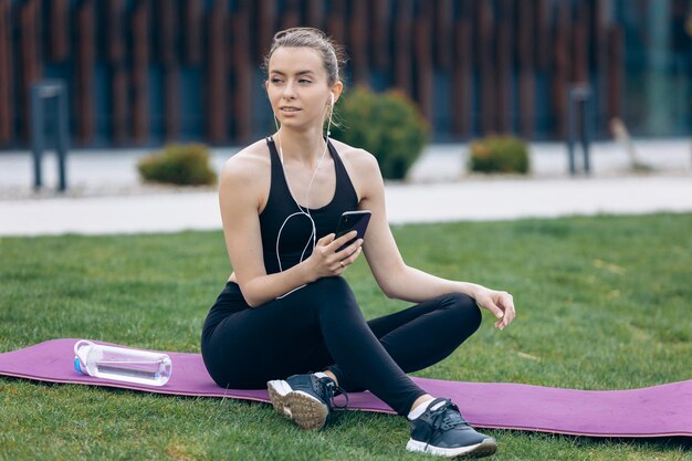 Fille blonde avec queue de cheval assis sur un tapis de yoga à côté