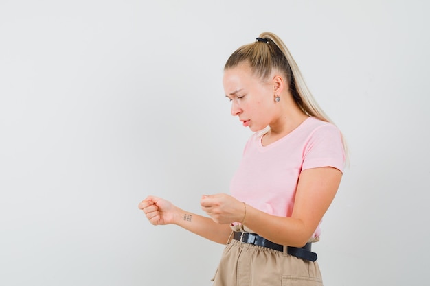 Photo gratuite fille blonde regardant quelque chose prétendait être tenue en t-shirt, pantalon et l'air abattu. vue de face.