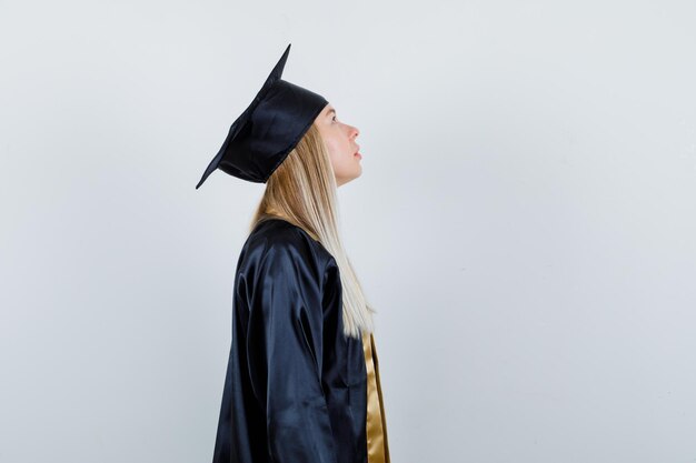 Fille blonde regardant vers le haut en uniforme de diplômé et regardant pensive.