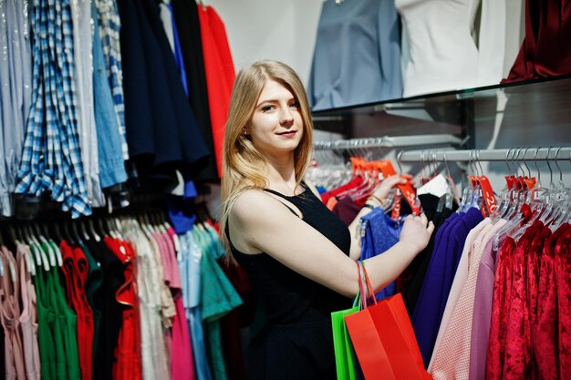 Une fille blonde avec des sacs à provisions choisit des vêtements dans la boutique