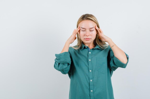 Fille blonde se frottant les tempes en blouse verte et ayant l'air fatigué.