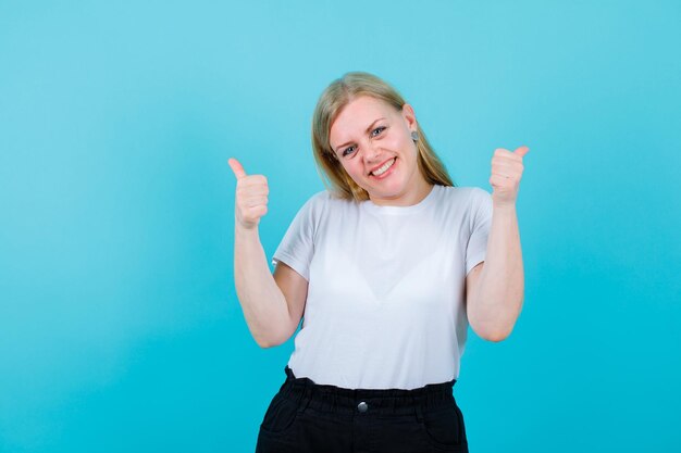 Une fille blonde souriante montre des gestes parfaits sur fond bleu