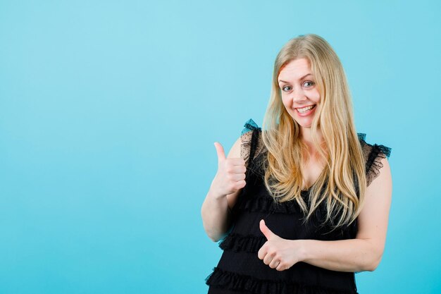 Une fille blonde souriante montre des gestes parfaits sur fond bleu