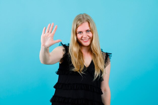 Une fille blonde souriante montre sa poignée sur fond bleu