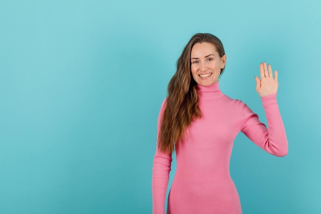 Une fille blonde sourit en levant la main sur fond bleu