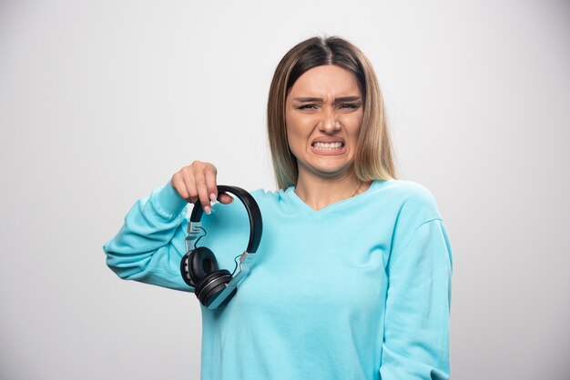 Fille blonde en sweat-shirt bleu écoute les écouteurs et n'apprécie pas la musique.