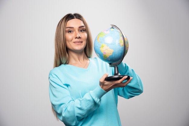 Fille blonde en sweat-shirt bleu tenant un globe, deviner l'emplacement et s'amuser.