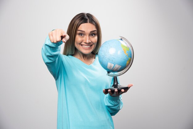 Fille blonde en sweat-shirt bleu tenant un globe, deviner l'emplacement et s'amuser.