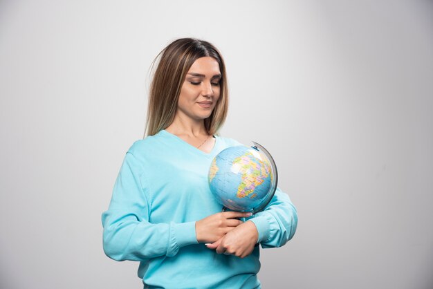 Fille blonde en sweat-shirt bleu tenant un globe, deviner l'emplacement et s'amuser.