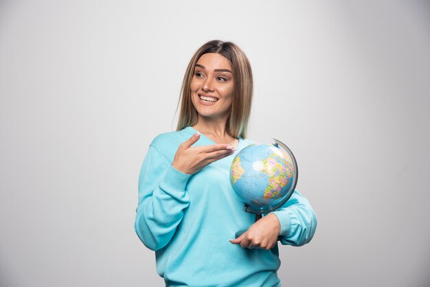 Fille blonde en sweat-shirt bleu tenant un globe, deviner l'emplacement et s'amuser.