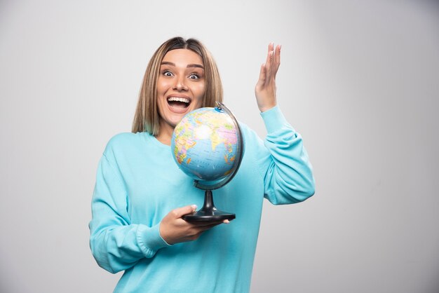 Fille blonde en sweat-shirt bleu tenant un globe, deviner l'emplacement et s'amuser