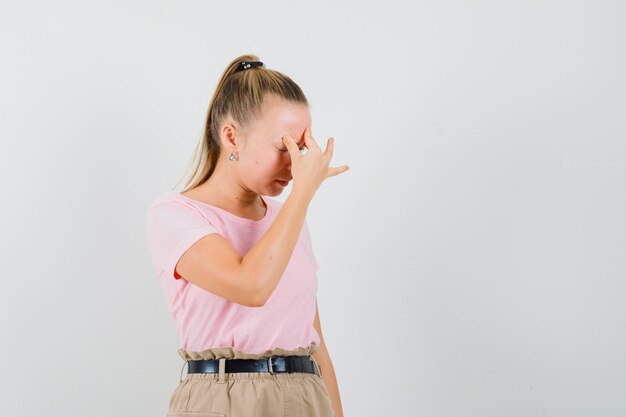 Fille blonde en t-shirt, pantalon frottant le front et à la colère, vue de face.