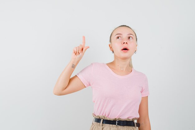 Fille blonde en t-shirt, pantalon pointant vers le haut et regardant curieux, vue de face.