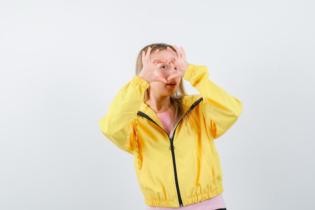 Fille blonde en t-shirt rose et veste jaune montrant un geste d'amour avec les mains et à la séduisante