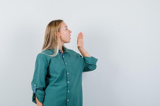 Fille blonde tenant la main près de la bouche comme appelant quelqu'un en blouse verte et à l'accent