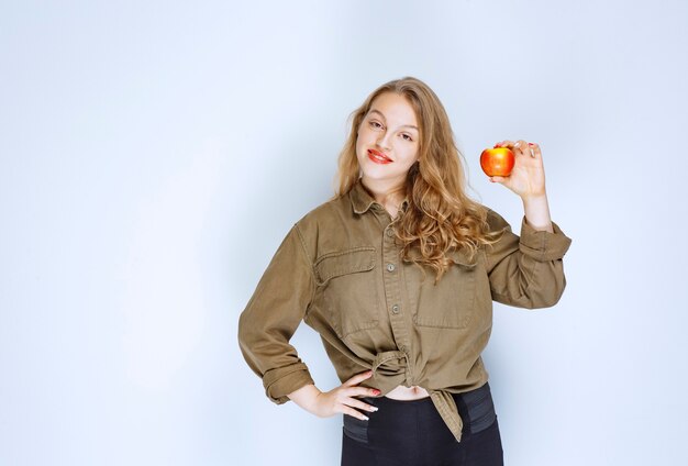 Fille blonde tenant et promouvant une pêche rouge.