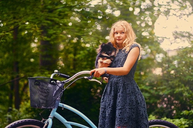 Fille blonde sur un vélo est titulaire d'un chien Spitz.