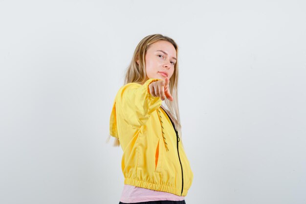 Fille blonde en veste jaune pointant vers la caméra et à la confiance