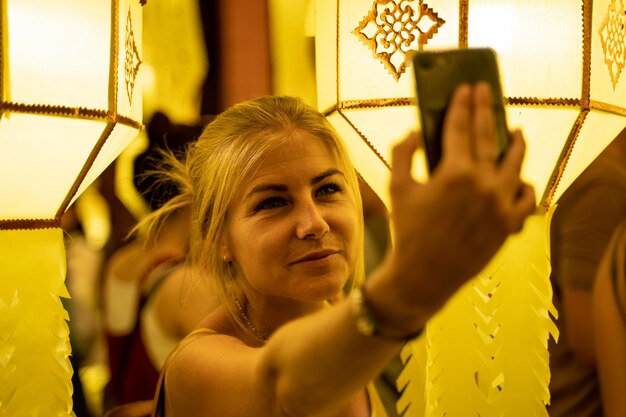 Fille blonde vêtue d'une robe bustier entourée de lanternes chinoises la nuit faisant un selfie