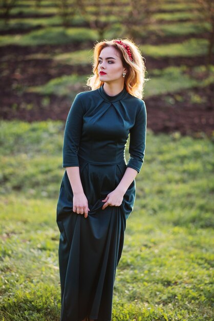 Fille blonde Yong élégance à robe verte sur le jardin au printemps au coucher du soleil