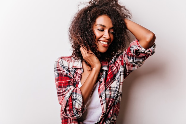 Fille bouclée détendue posant avec un sourire heureux. portrait de jeune femme africaine bien habillée.