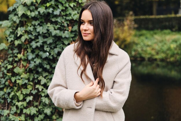 Fille brune assez élégante en manteau regardant rêveusement loin en plein air