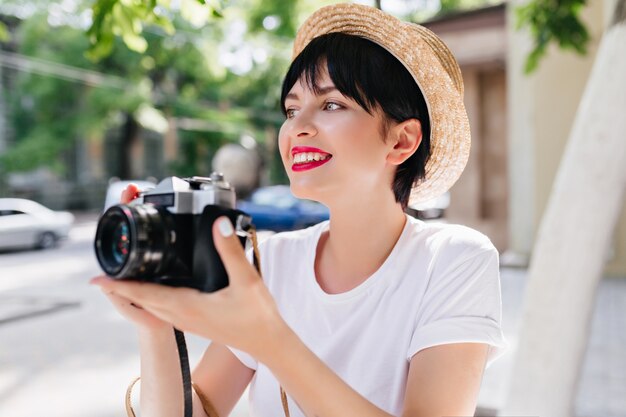 Fille brune extatique avec professionnel à la recherche de suite en souriant, profitant d'une vue imprenable sur la nature