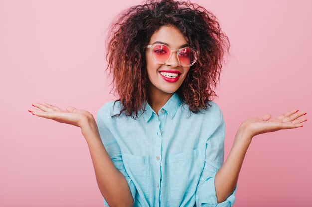 Fille brune heureuse avec un sourire surpris posant avec les mains vers le haut. Charmante femme mulâtre à la peau de bronze exprimant de bonnes émotions.