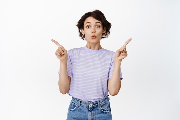 Une fille brune intriguée dit wow, l'air étonné, pointant les doigts sur le côté pour copier l'espace sur blanc.