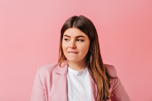 Fille brune sensuelle en détournant les yeux. Belle jeune femme aux cheveux raides debout sur fond rose.