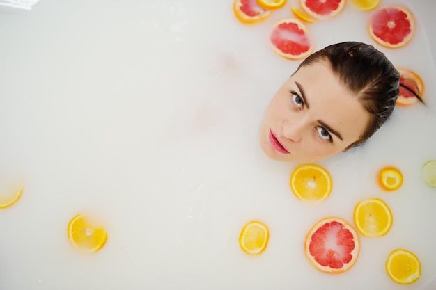 Fille brune sexy à la salle de bain avec du lait et des fruits Bain de jeunesse pour le corps