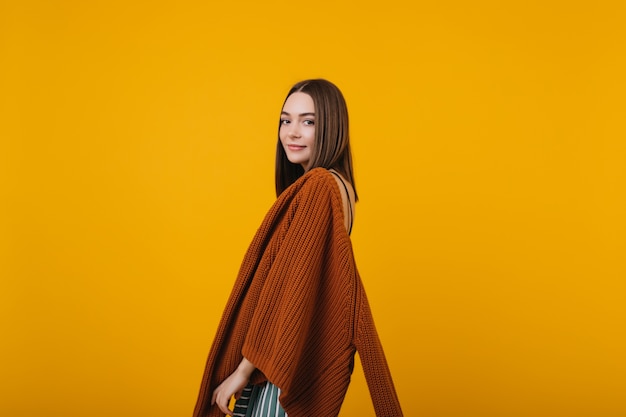 Fille brune timide posant en pull tricoté marron. Portrait intérieur d'une femme européenne intéressée isolée.