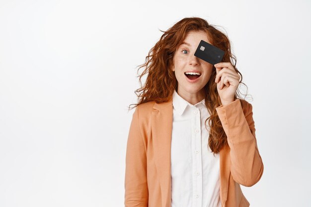 Une fille de bureau excitée montre une carte de crédit et des sourires étonnés recommande des stands de banque en costume sur fond blanc