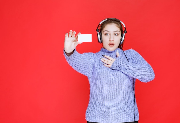 Fille avec un casque tenant une carte de visite et a l'air surprise.