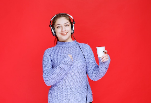 Fille avec un casque tenant une tasse de café jetable.